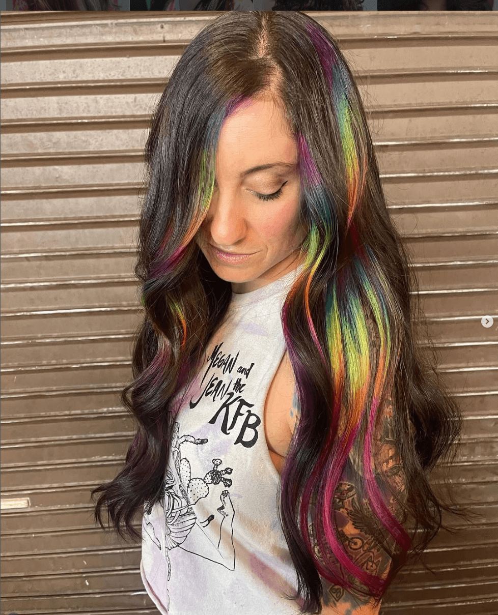 Rainbow peekaboo highlights with pink, teal, and yellow woven through natural brunette waves